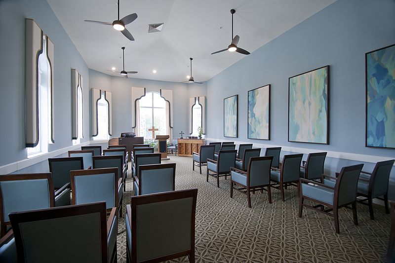 A neatly arranged meeting room with chairs facing a podium, ceiling fans, and artwork on the walls.
