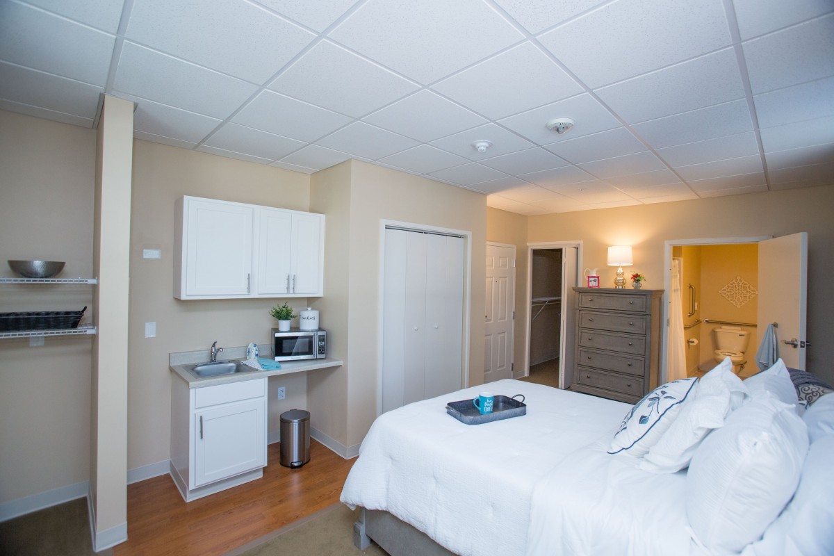 A modern and tidy bedroom featuring a bed, dresser, and a small kitchenette.