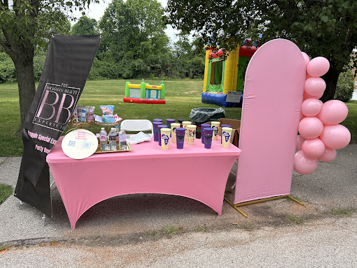 A beautifully arranged pink table setup for an outdoor event, complete with decorations and fun activities in the background.