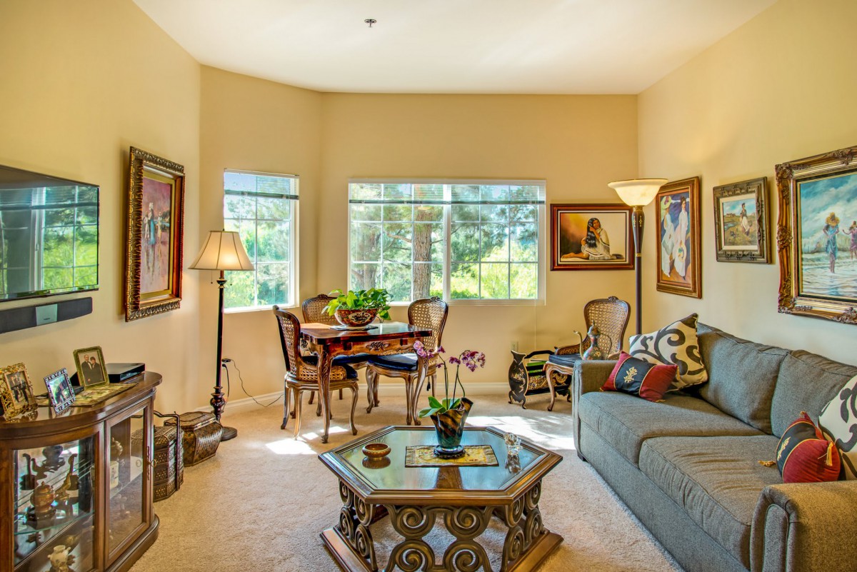 A cozy living room with elegant furniture and decorative artwork, featuring a comfortable sofa and a dining area by the windows.