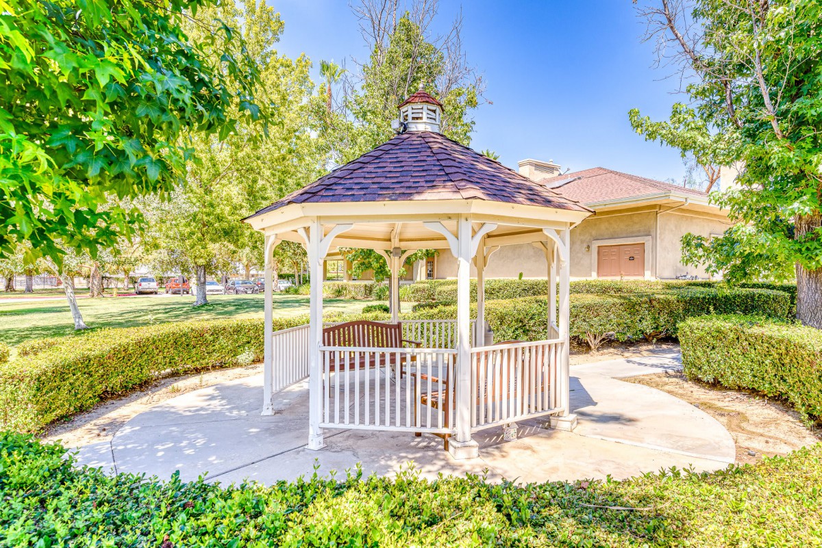 A charming wooden gazebo surrounded by lush greenery on a sunny day in a park setting.