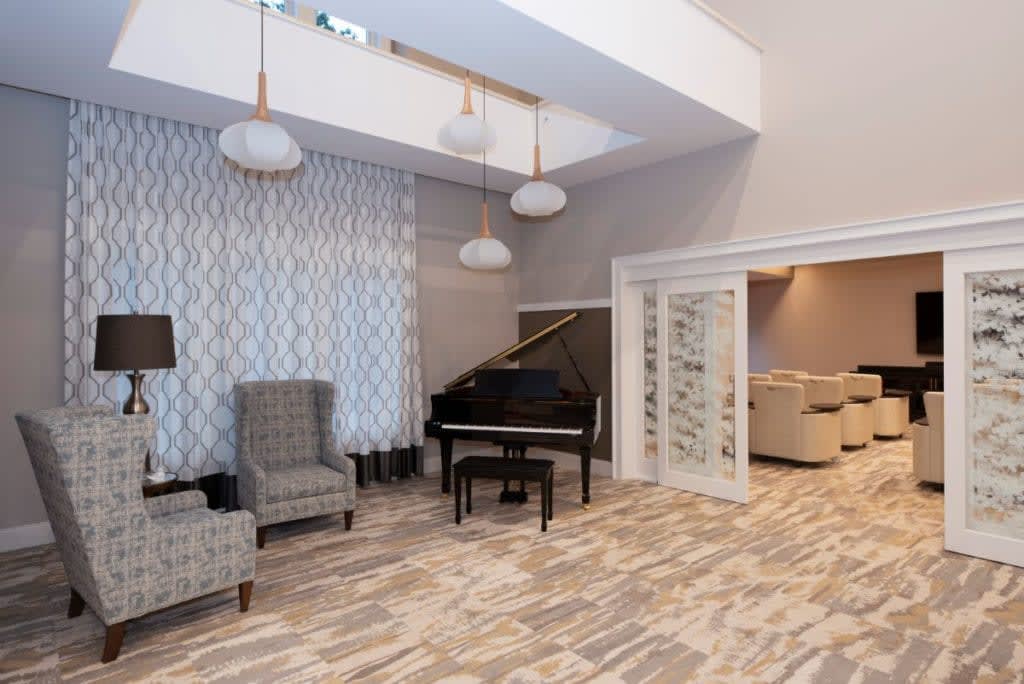 A modern living room with a grand piano, stylish armchairs, and elegant chandeliers.