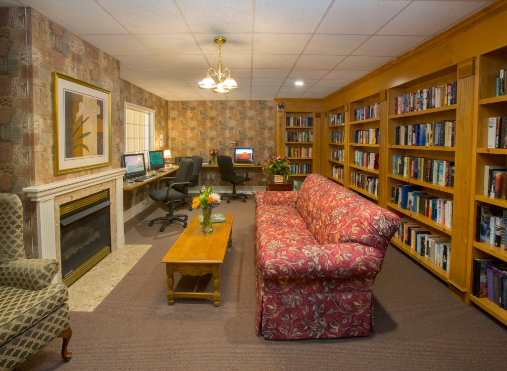 A cozy library with bookshelves, a sofa, computer desks, and a fireplace.