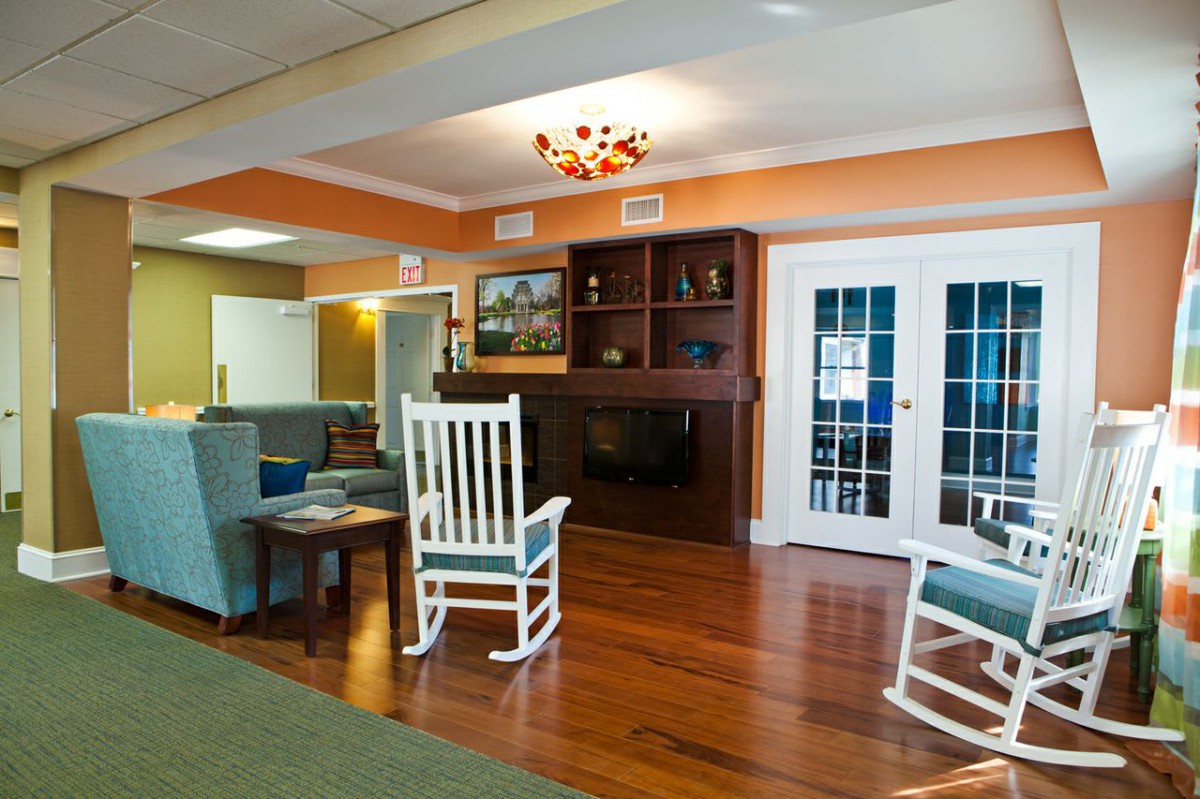 A cozy living room with a wooden floor, featuring a rocking chair, bookshelf, and fireplace.