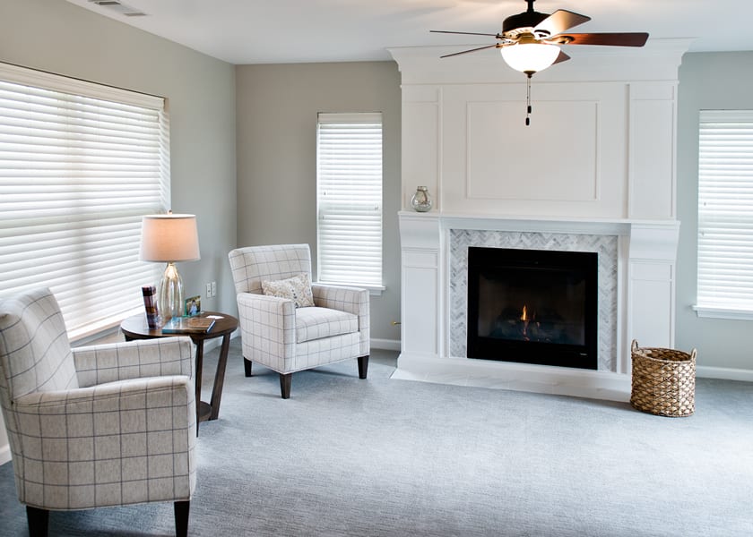 A modern living room featuring a cozy fireplace, armchairs, and natural light from two windows.