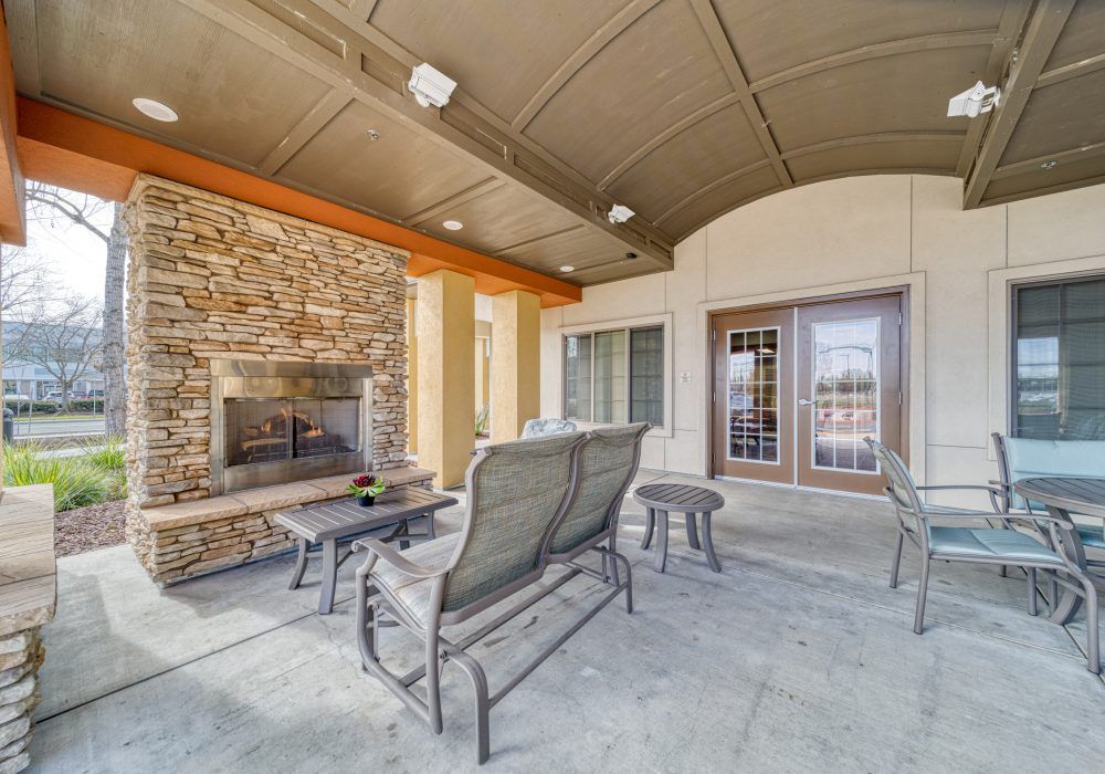A cozy outdoor patio with comfortable seating and a stone fireplace under a covered roof.