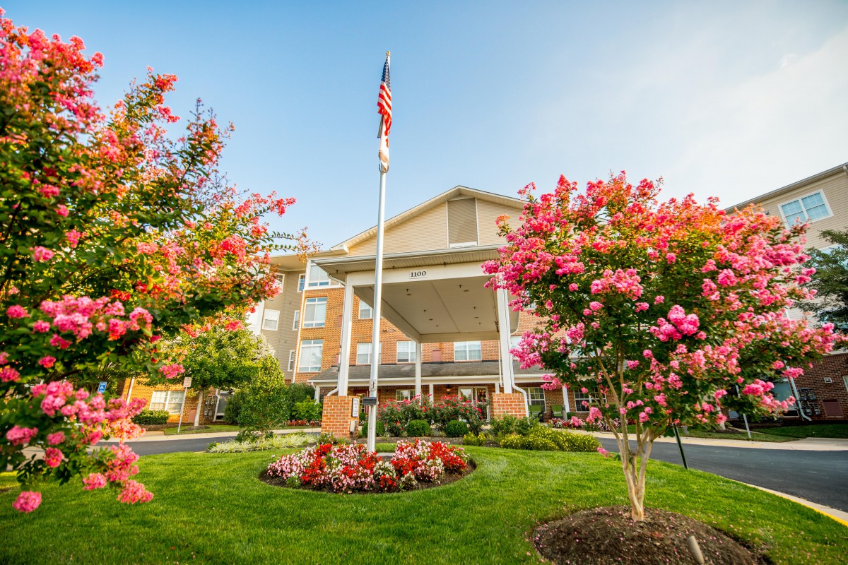 A building with a well-maintained garden featuring colorful flowers and trees, accompanied by a flagpole displaying the American flag.