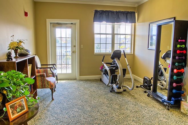 A cozy exercise room with a stationary bike, armchair, and large windows.