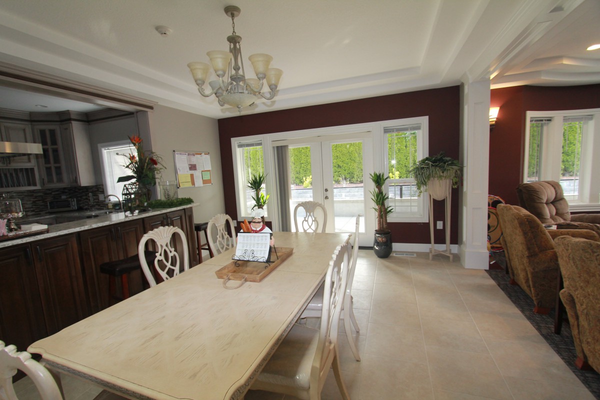 A well-lit dining room with a large table and elegant chairs, complemented by a chandelier and indoor plants.