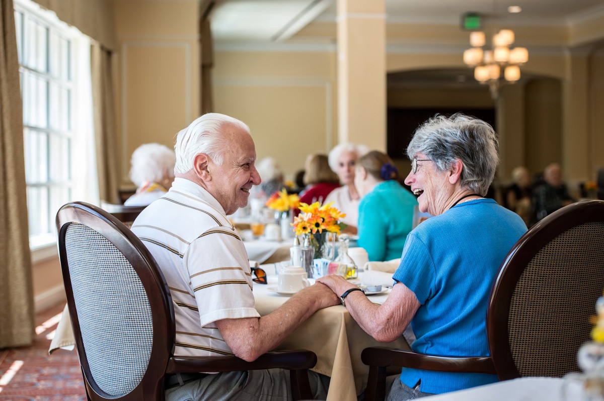 A group of seniors enjoying a meal and conversation in a communal dining area.