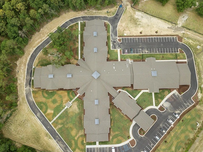 Aerial view of a cross-shaped building with surrounding landscape and parking area.
