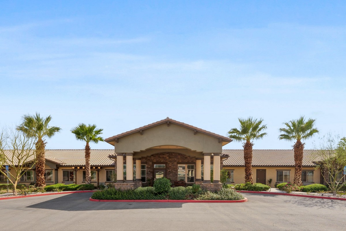 A large building with a prominent entrance, surrounded by palm trees under a clear sky.