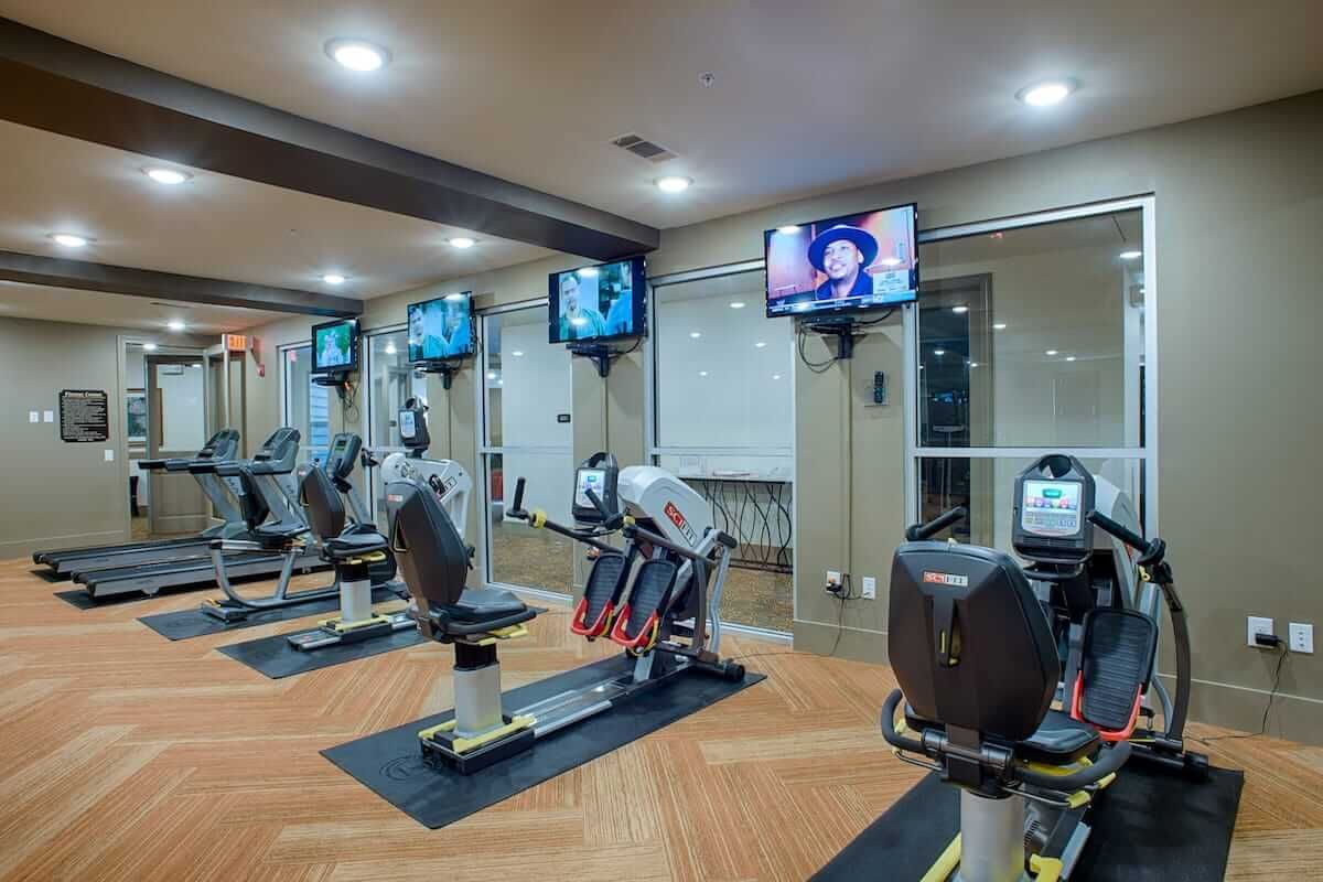 A modern gym equipped with cardio machines and televisions.