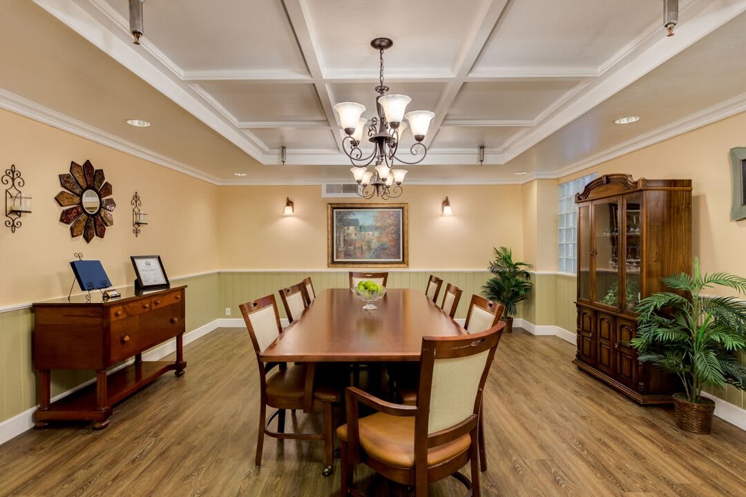 A well-designed dining room featuring a large wooden table with chairs, illuminated by an elegant chandelier. The room is adorned with wall art and decorative plants, accentuating the classic ceiling design.