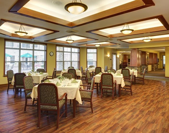 A well-lit dining area with neatly arranged tables and chairs, featuring wood flooring and elegant lighting.