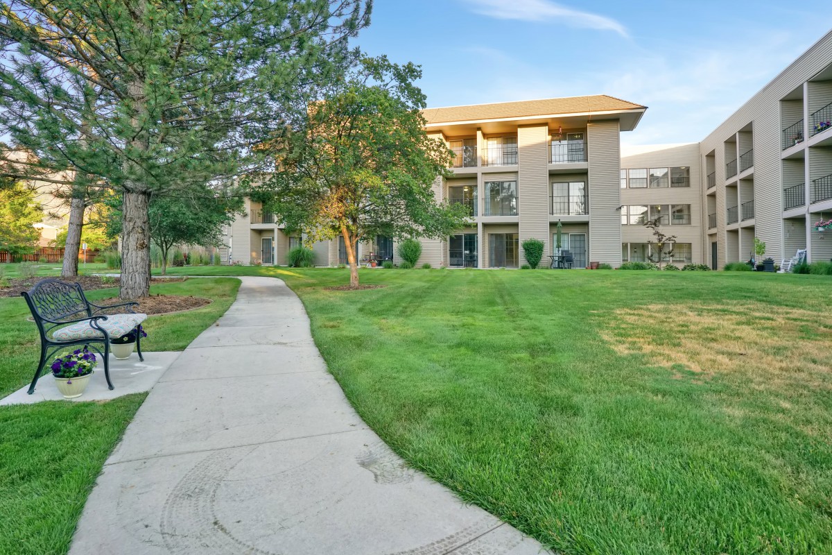 A scenic view of an apartment complex with a lush green lawn and pathway.