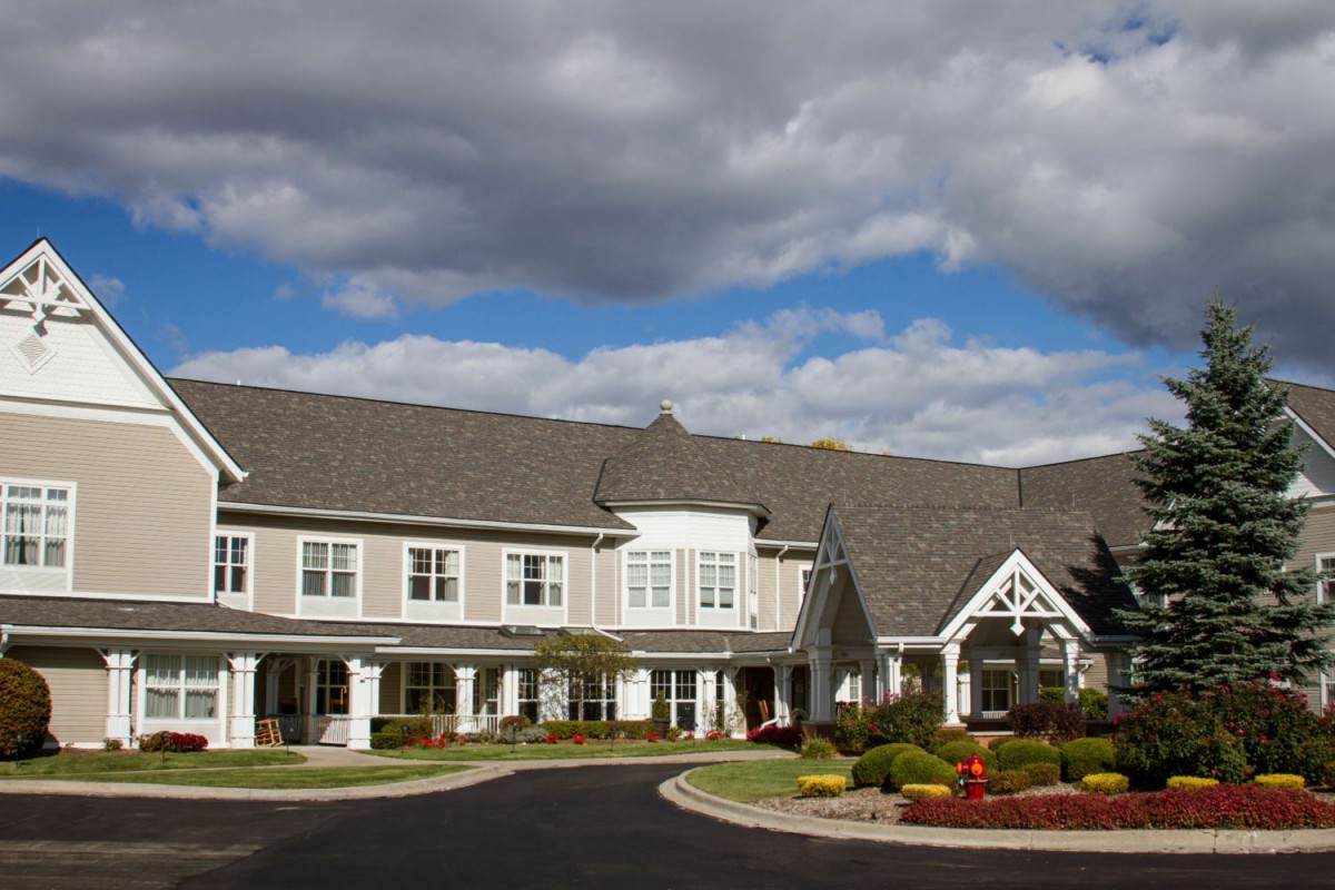 A large, two-story residential building under a partly cloudy sky.