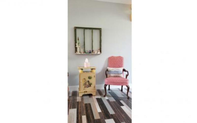A cozy interior featuring a vintage chair, a small decorative table with a lamp, and a wall shelf.