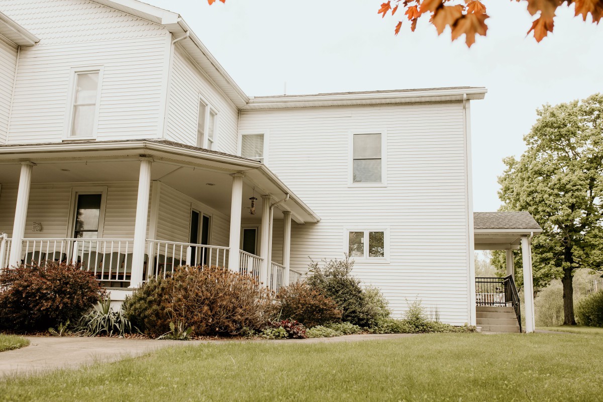 A suburban white house with a porch and a well-kept front yard, framed by autumn leaves.
