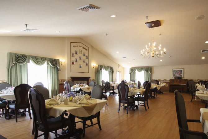 A spacious and elegant dining room with tables set for service, featuring a chandelier and large windows.