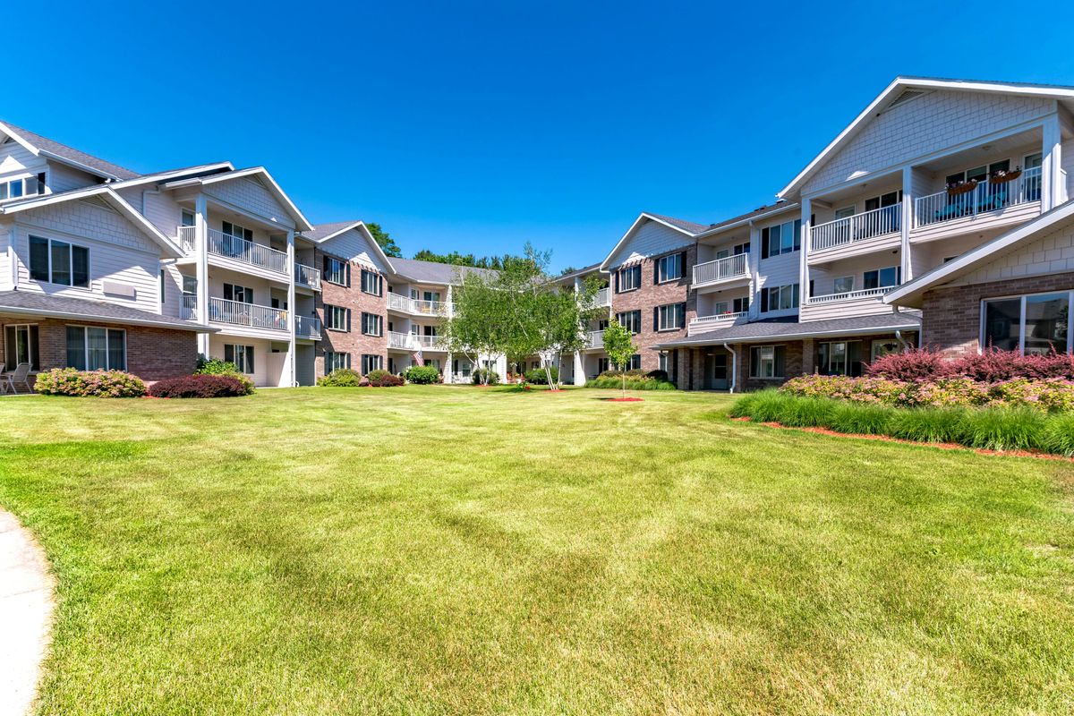 A view of residential apartment buildings surrounding a well-maintained lawn under a clear blue sky.