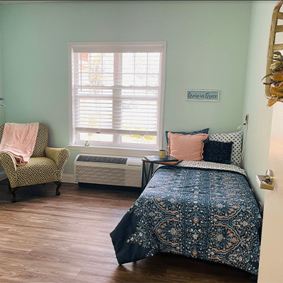 A cozy bedroom with a bed, armchair, and window letting in natural light.