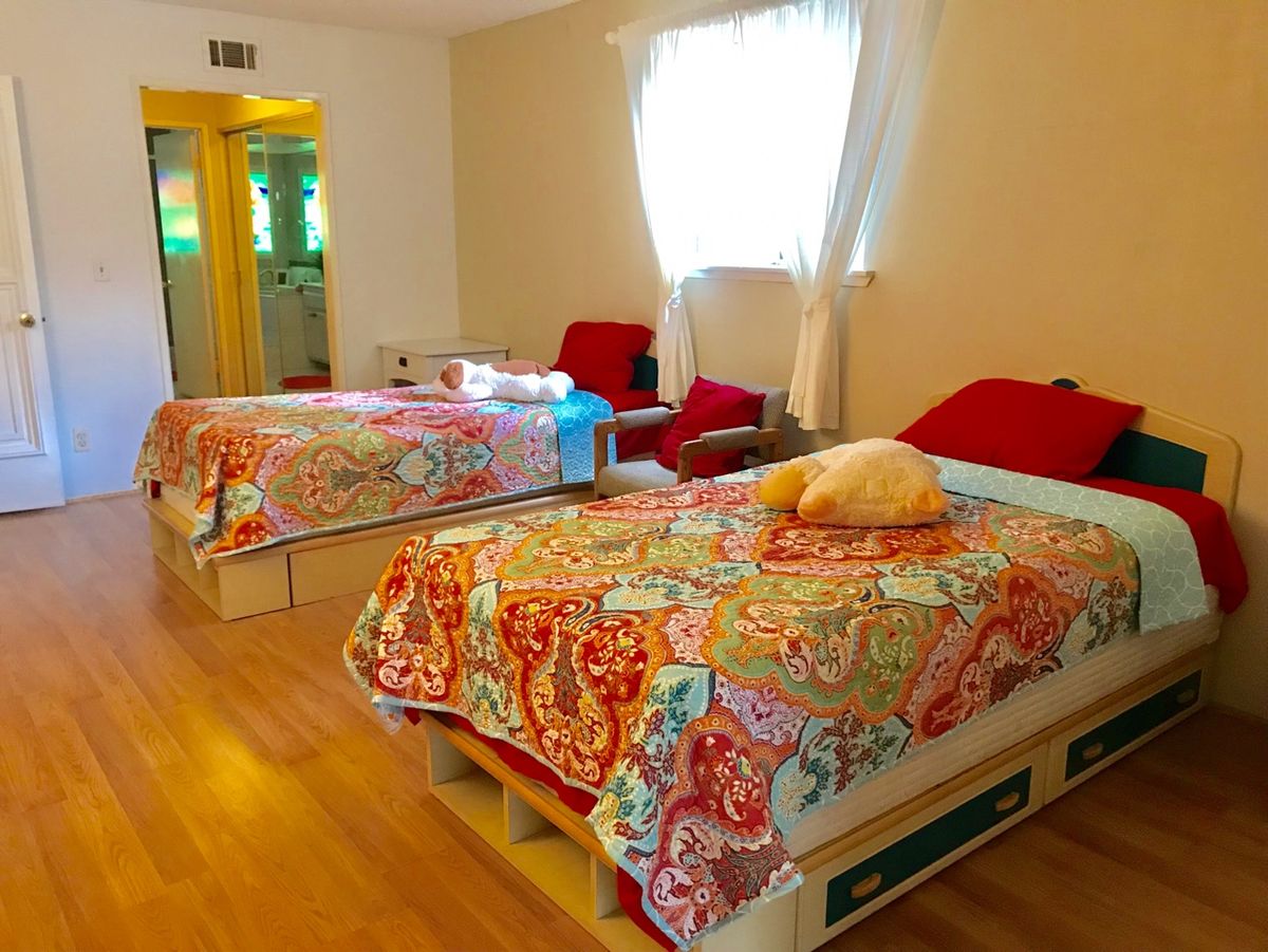 A cozy bedroom featuring two beds with colorful bedding and matching pillows on a wooden floor.