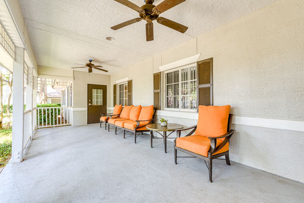 A spacious patio with orange-cushioned chairs, ceiling fans, and large windows.