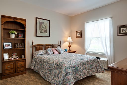 A cozy bedroom with a wooden bed, patterned bedding, and a lamp by the window.