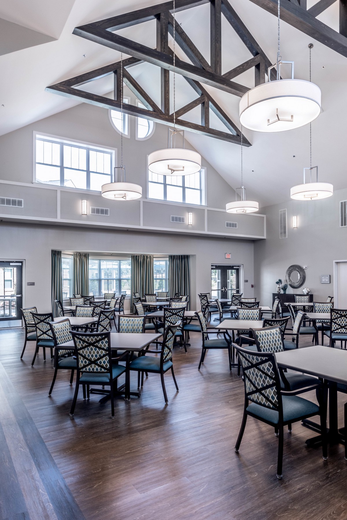 A spacious and bright dining area with multiple tables, chairs, and elegant chandeliers.
