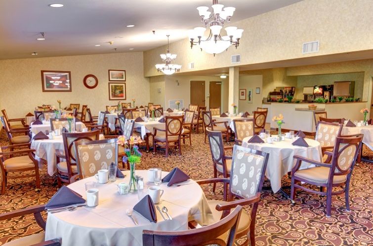 A well-lit dining room with neatly arranged tables and elegant chandeliers.