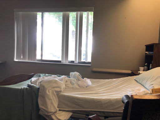 A hospital room with an unmade bed and natural light coming through the windows.