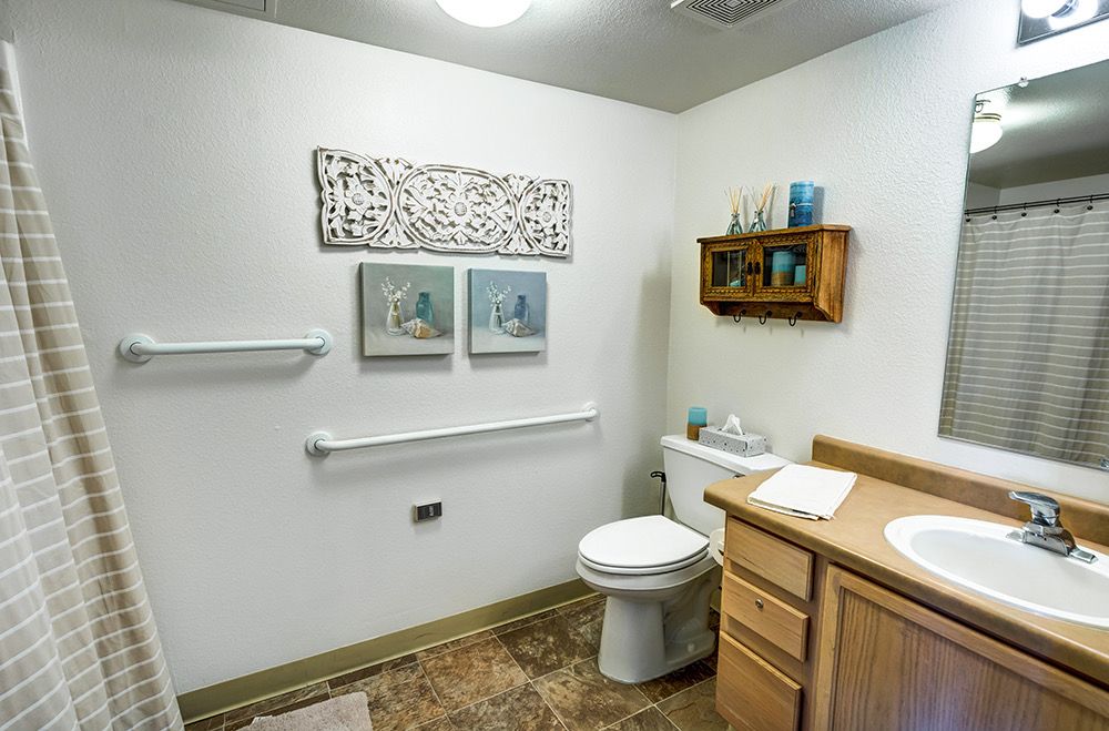 A well-organized bathroom featuring a toilet, sink, shelving with towels and toiletries, and decorative artwork on the walls.