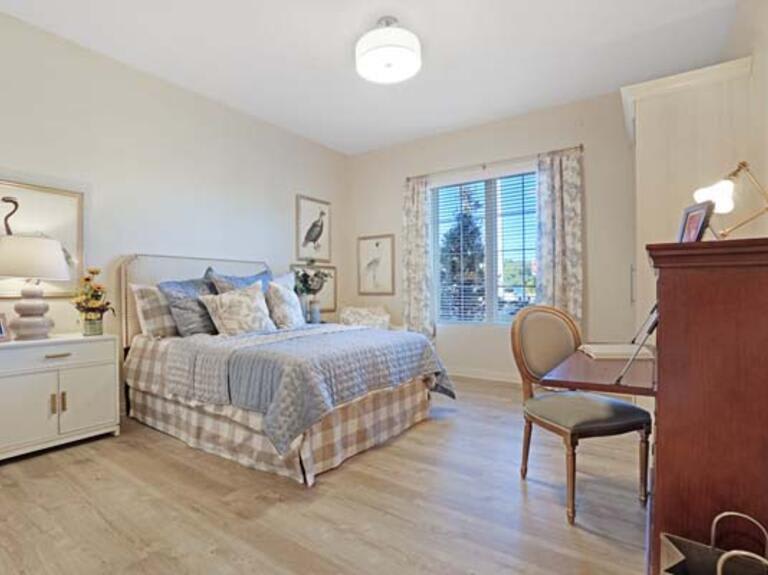 A cozy and well-decorated bedroom with a large bed, a desk with a chair, and natural light coming through the window.