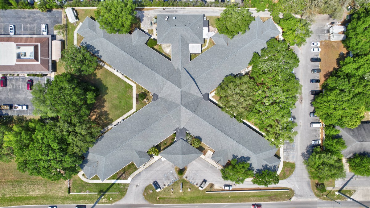 Aerial view of a large building with a distinctive X-shaped layout, surrounded by trees and a parking lot.