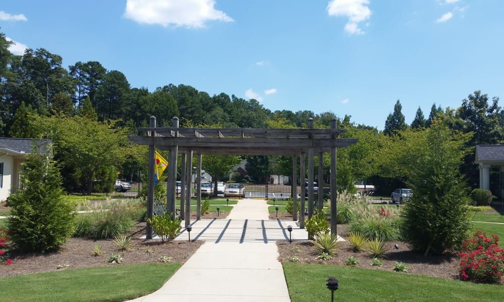A sunny day in a beautifully landscaped garden featuring a pergola over a pathway.