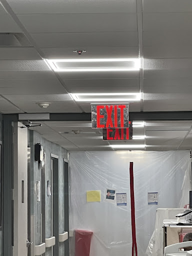 A view down a hallway featuring an illuminated exit sign and plastic barriers, indicating ongoing renovation work.