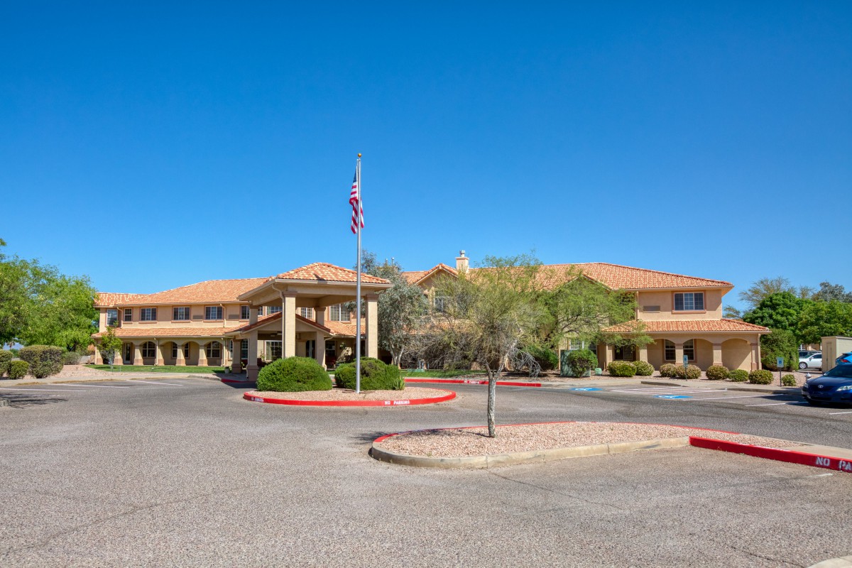 A wide-angle view of a large building with an American flag, surrounded by landscaping and a paved driveway under a clear blue sky.