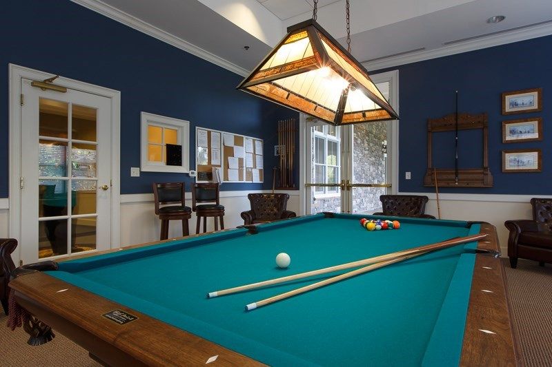 A stylish game room featuring a pool table with cue sticks under a rustic lighting fixture.