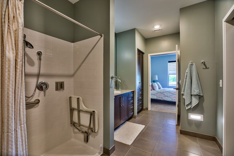 A modern bathroom with a large shower and sleek fixtures, leading into a bedroom.
