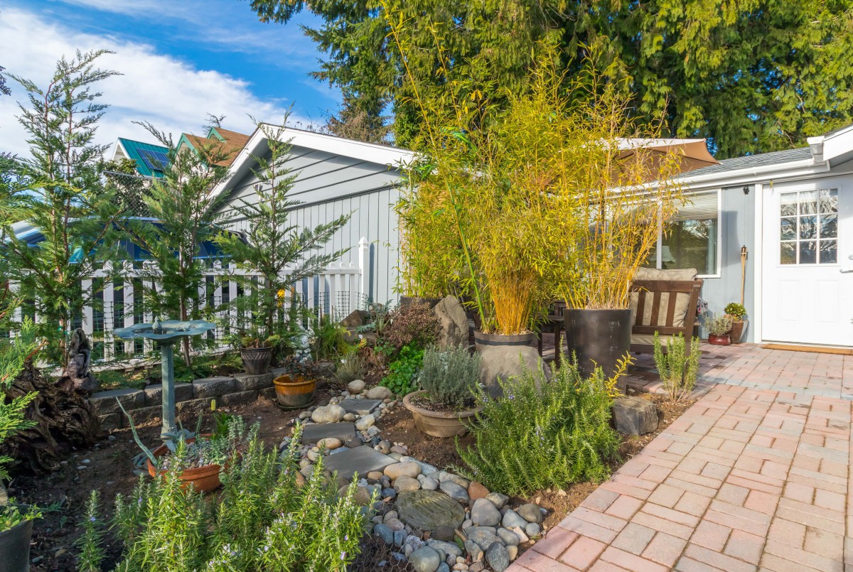 A beautifully landscaped garden with a variety of plants and a paved pathway beside an outdoor seating area.