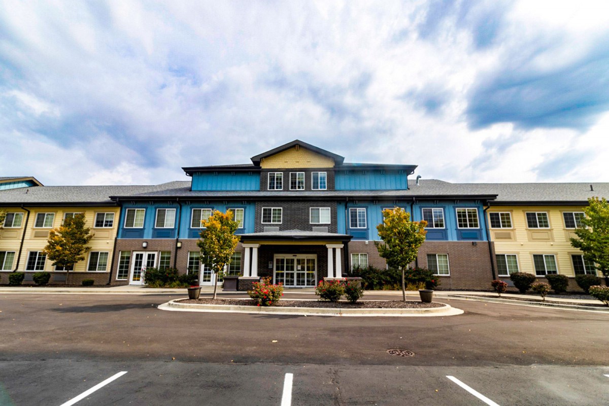 A modern residential building with a parking lot and trees at the front.