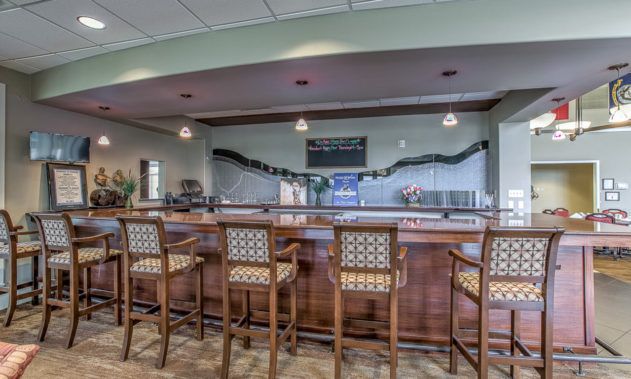 An indoor bar area featuring a wooden counter and high-backed chairs.