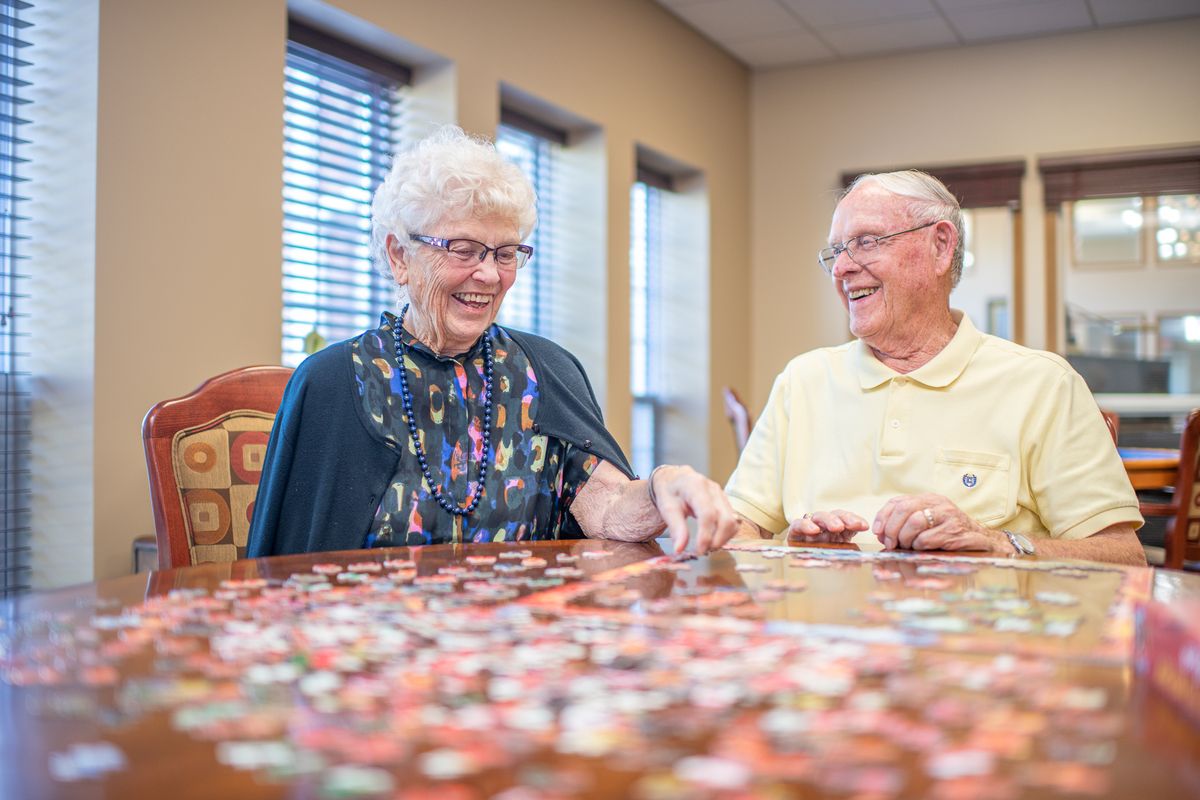 Two elderly individuals enjoying a puzzle together indoors.