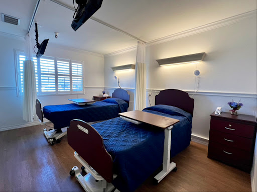 A well-lit hospital patient room with two adjustable beds and a warm, inviting atmosphere.