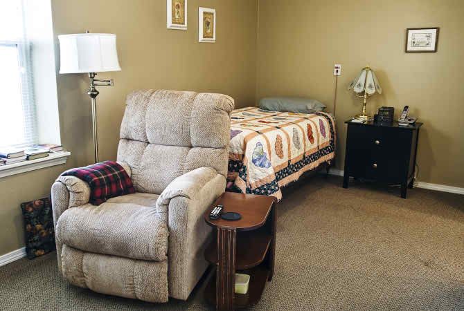 A cozy bedroom with a recliner chair, bed, lamp, and nightstand.