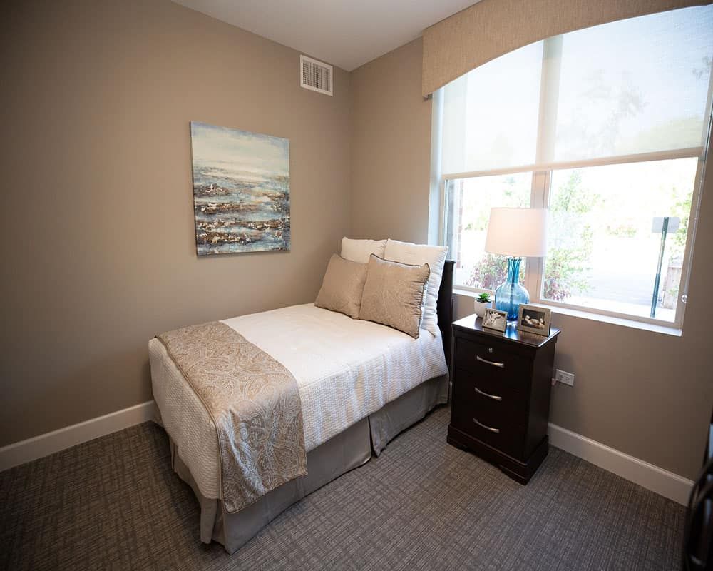 A cozy bedroom with a single bed, nightstand, and window.