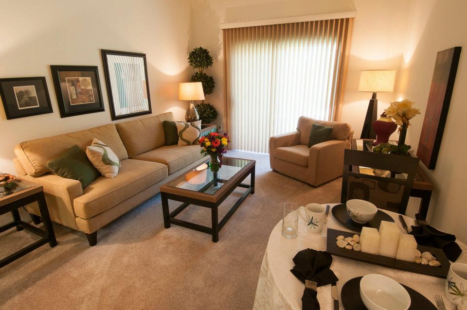 A cozy and well-decorated living room featuring a sofa, armchair, coffee table, and dining area with warm lighting.