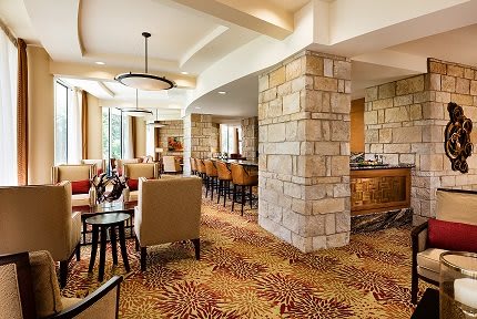 A modern hotel lounge featuring comfortable seating, stone walls, and a bar counter with ample natural lighting.