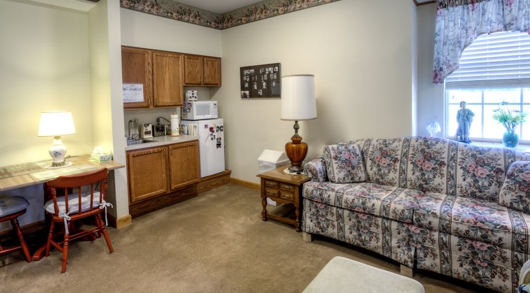 A cozy living space with a kitchenette, featuring floral-patterned furniture and warm lighting.